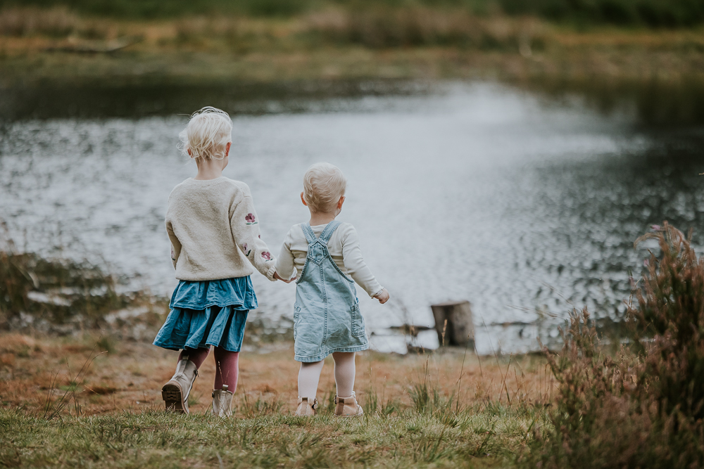 Fotograaf Friesland. Twee zusjes lopen hand in hand naar het vennetje toe. Gezinsshoot Appelscha door Nickie Fotografie.