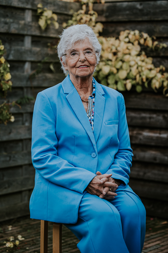 Fotograaf Dokkum. Portret van dame in blauw pak zittend op een kruk voor de schutting. Fotoshoot door Nickie Fotografie uit Friesland.