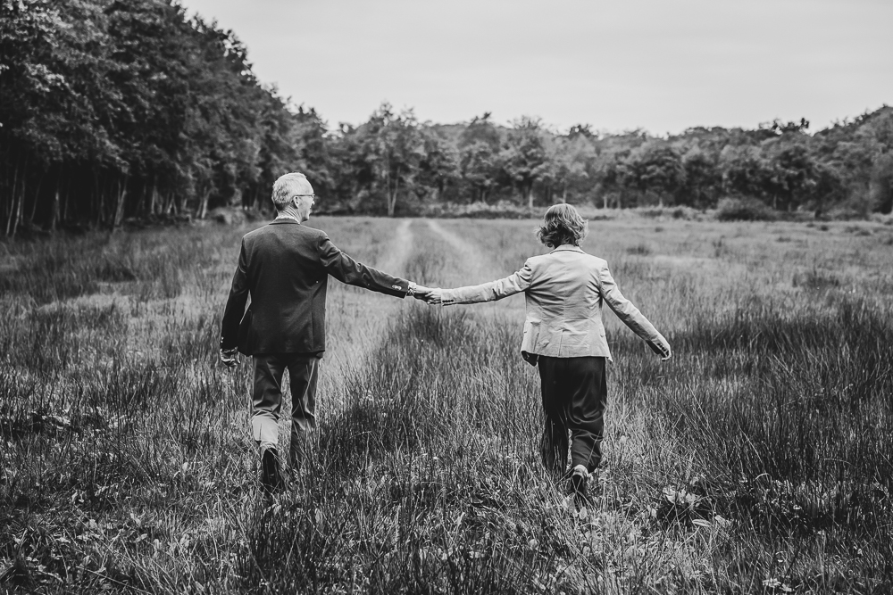 Fotograaf Friesland. Zwart-wit portret van de ouders, hand in hand lopend door het veld door Nickie Fotografie.