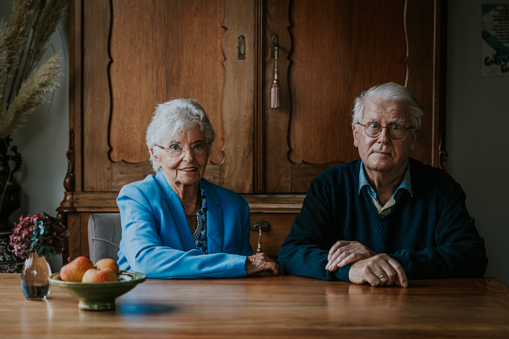 Senioren fotografie Dokkum. Portret van ouder echtpaar bij hun thuis voor de antieke kast door fotograaf Nickie Fotografie.