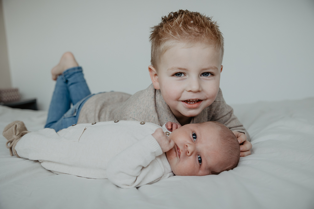 Fotograaf Friesland. Babyreportage door Nickie Fotografie. Trotse grote broer poseert op het grote bed mijn zijn babybroertje.