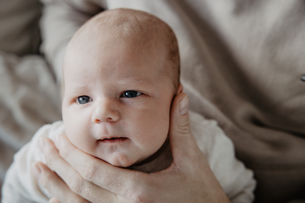 Babyfotografie Friesland. Vader houdt het hoofdje van het babytje vast. Het kleintje kijkt de wereld in. Newbornfotografie door fotograaf Nickie Fotografie uit Dokkum.