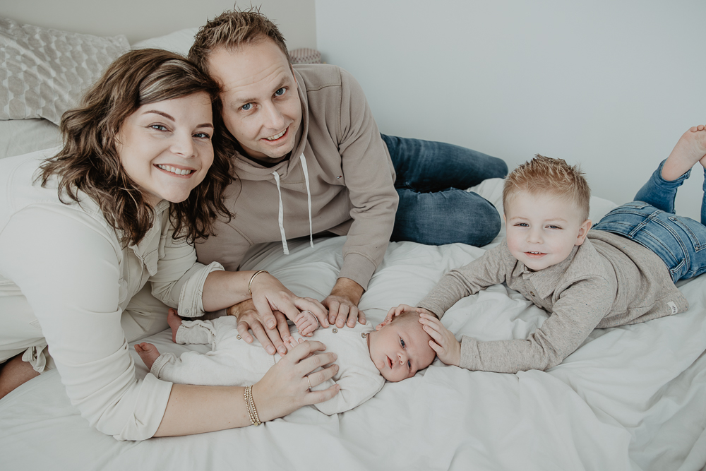 Speels gezinsportret met pasgeboren baby op het ouderlijke bed. Gezinsshoot door fotograaf Nickie Fotografie uit Friesland.