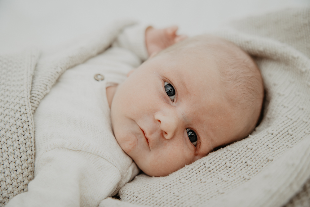 Fotograaf Dokkum. Newbornshoot door Nickie Fotografie. Portret van de kleine lekker ingewikkeld in de gebreide deken.