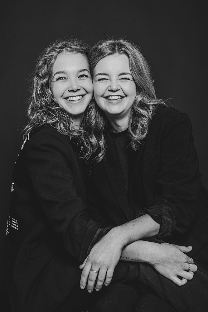 Studioportret Friesland. Vrolijk dubbelportret van 2 zussen in het zwart gekleed door fotograaf Nickie Fotografie uit Dokkum.