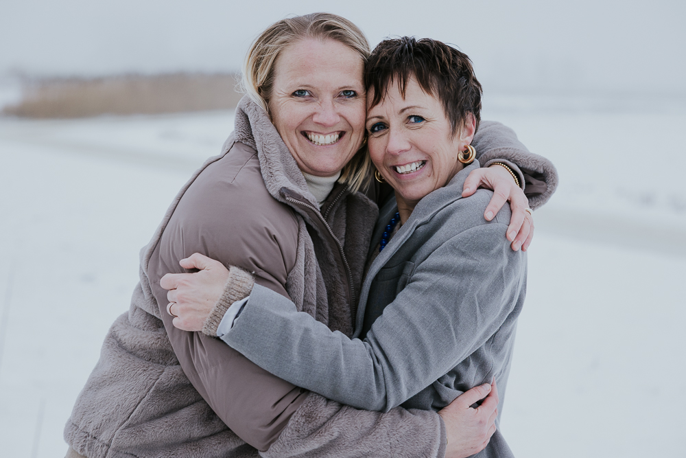 Vriendinnenshoot in de sneeuw. Gezellig knuffelportret in het weiland door fotograaf Nickie Fotografie uit Dokkum, Friesland.