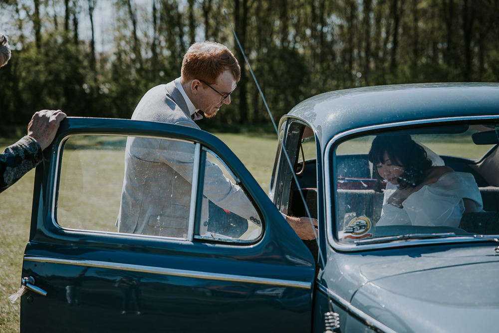 Bruidegom helpt zij bruid uit de auto stappen. Trouwshoot door fotograaf Nickie Fotografie.