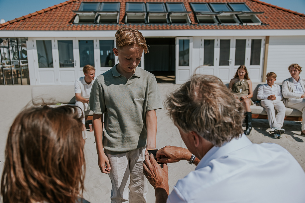 Zoon van het bruidspaar overhandigt de trouwringen tijdens de huwelijksceremonie op het strand bij Hollum. Bruidsreportage door fotograaf Nickie Fotografie uit Friesland.